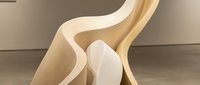 Large organic sculptural form with smooth flowing curves in warm beige tones displayed in a contemporary gallery space.
