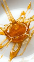 Golden honey or oil splashing dynamically with droplets and streams frozen in motion against a white background, suitable for food, cosmetics, wellness and beverage marketing.