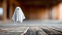 Classic ghost figure with white sheet floating above rustic wooden floor in blurred interior space, creating spooky Halloween atmosphere.