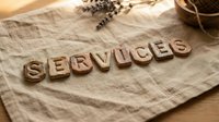 Rustic wooden letter tiles spelling SERVICES on linen fabric with lavender and twine, warm natural tones for business and branding concepts.
