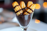 Chocolate dessert served in martini glass with mini cannoli pastries dipped in dark chocolate sauce, garnished against blurred bokeh lights background.