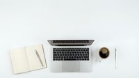 Modern workspace flat lay with open laptop, blank notebook, pen and coffee cup on clean white background for business and productivity concepts.
