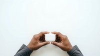 Two hands with medium-dark skin tone holding a blank white rectangular card or product mockup against neutral background for branding and marketing purposes.