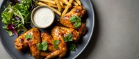 Grilled chicken wings with golden french fries, fresh salad and creamy dipping sauce served on dark plate. Restaurant meal ready for dining and food delivery.