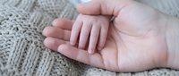 Tiny newborn hand resting gently in a parent's palm on a soft knit blanket, symbolizing love, care, and new life.