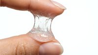 Stretchy clear gel or slime being pulled between fingers on white background, demonstrating elasticity and texture for product, science, or sensory play content.