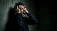 Stressed middle-aged Caucasian businessman in dark suit holding head in hands, screaming in anguish against concrete wall. Mental health crisis concept.