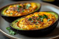 Baked avocado halves filled with eggs and cheese, garnished with fresh herbs on ceramic plate. Healthy breakfast or brunch recipe for ketogenic diet.
