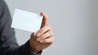 Close-up of male hand holding blank white business card against neutral background. Professional mockup for corporate branding and identity design.