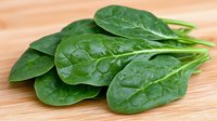 Fresh raw spinach leaves with water drops arranged on wooden cutting board, healthy organic green vegetable for cooking and salads, macro food photography.