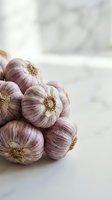 Fresh purple garlic bulbs clustered together on white marble surface with soft natural light, suitable for food photography, cooking blogs, and culinary content.