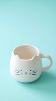 Adorable white ceramic cat mug with whiskers and ears on mint green background for kitchen decor and beverage serving.