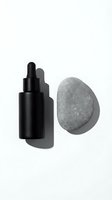 Black dropper bottle with natural gray stone on white background for skincare cosmetics branding and spa wellness product photography.