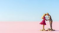 Romantic couple holding heart symbol on pink salt lake with blue sky background for wedding and love concepts.