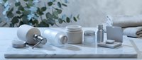 Minimalist skincare cosmetic products arranged on white marble surface with eucalyptus leaves. Clean beauty routine essentials for spa wellness.