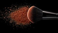 Makeup brush with explosion of coral color loose powder against black background, creating dynamic cosmetic motion effect for beauty and fashion concepts.
