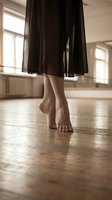 Woman dancing barefoot on wooden floor in flowing black dress at bright studio with natural window light for dance and movement concepts.