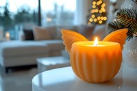 Orange butterfly-shaped candle glowing warmly on white table in cozy living room with Christmas decorations and bokeh lights creating festive holiday atmosphere.