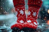 Red knitted wool socks with white snowflake pattern standing in rain puddle. Cozy winter footwear against blurred turquoise background with falling water drops and bokeh lights.