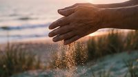 Close-up of hands releasing sand at beach during golden hour sunset, capturing motion and texture for travel, wellness, and lifestyle concepts.