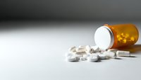 Orange prescription bottle with white pills spilled on clean surface for healthcare and medication concepts.
