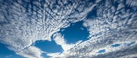 Dramatic altocumulus cloud formation creating natural patterns across bright blue sky with white fluffy clouds scattered throughout atmospheric landscape.