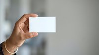 Hand holding blank white business card against blurred office background, suitable for branding, corporate identity, and professional marketing materials.