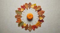 Autumn leaves arranged in circular wreath pattern with orange pumpkin centerpiece on neutral background for seasonal decoration and harvest themes.