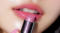 Pink glossy lipstick application close up on Asian woman lips showing perfect white teeth and shiny makeup product for beauty and cosmetics advertising.