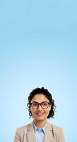 Young woman with dark curly hair and glasses wearing beige blazer over light blue shirt, smiling at camera against plain light blue background for corporate headshot or professional portrait use.