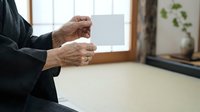 Senior man in dark business suit holding blank white card with both hands, displaying empty space for text or branding in modern office setting.