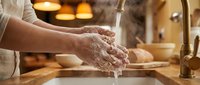 Elderly woman washing hands thoroughly with soap and water at kitchen sink in warm home environment for hygiene and health safety practices.