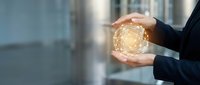Business professional hands protecting glowing digital network sphere in modern office environment representing cybersecurity and data protection concepts.