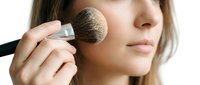 Woman applying powder blush with makeup brush to cheek, beauty cosmetics and facial contouring technique for professional makeup application.