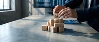 Businessman building wooden block tower on desk in modern office, representing strategic planning, growth, and business development concepts.