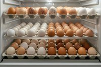 Variety of fresh eggs in different shades stored in refrigerator shelves, including white, brown, and speckled varieties for cooking and baking.