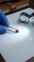 Gemologist in blue gloves holding a red ruby with tweezers under loupe magnification on a white surface for quality inspection.