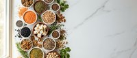 Variety of legumes, grains and seeds in bowls on marble background. Healthy protein sources including lentils, beans, chickpeas and nuts for vegetarian diet.