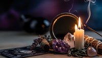Mystical fortune telling setup with burning candle, tarot cards, amethyst crystals and pine cones creating atmospheric scene for spiritual practices.