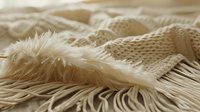 Soft beige knitted textile with fringe detail and cozy wool texture creates gentle layers and folds in neutral tones, suitable for fashion and home decor backgrounds.