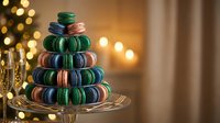Colorful macaron tower on glass stand with warm Christmas lights bokeh background creating festive holiday dessert display for celebrations and parties.