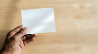 Cropped hand holding blank white card against wooden surface for branding, mockup, or business presentation purposes.