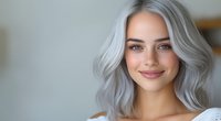 Young woman with trendy silver gray wavy hair and natural makeup smiling warmly at camera against light background, modern beauty portrait.
