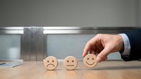 Businessman hand selecting happy face emoticon from sad to satisfied faces on wooden desk for customer service feedback rating concept.