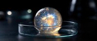 Transparent glass sphere with glowing energy burst inside sitting on reflective surface in dark laboratory setting with bokeh lights in background.