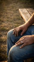 Senior man hands resting on knees while sitting on wooden bench outdoors in warm sunlight for relaxation and contemplation concepts.
