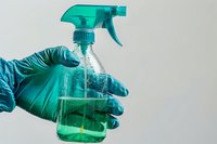 Hands in protective gloves holding green spray bottle for cleaning and disinfection on neutral background for hygiene and sanitation concepts.