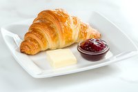 Fresh baked croissant served on white plate with butter pat and red berry jam for breakfast or brunch menu presentation.
