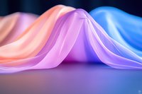 Smooth flowing fabric in pastel pink, purple and blue creates gentle waves and folds against dark background, showcasing soft textile movement and elegant draping.