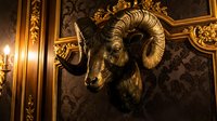 Ornate golden ram head sculpture mounted on dark damask wallpaper with decorative gold trim and candlelight, creating luxurious interior design and baroque home decor.